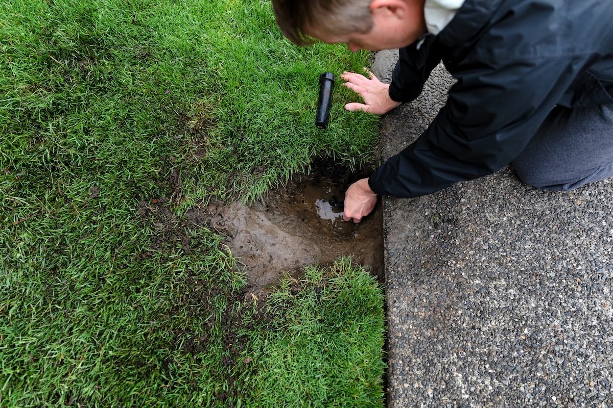 Sprinkler system being repaired by mature man with parts laying on ground
